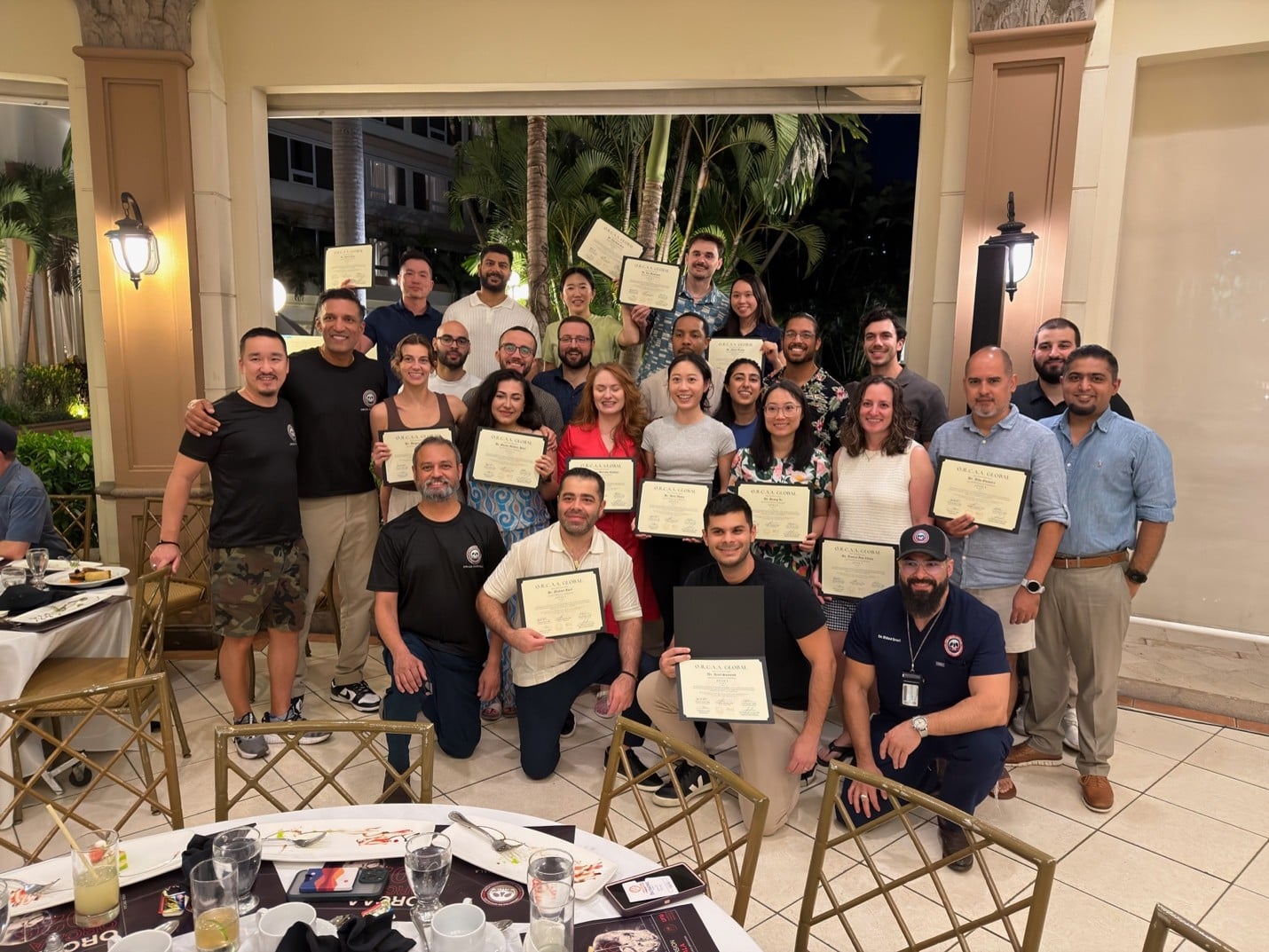 A large group of Lightwave doctors and ORCAA faculty smiling and holding up their implant training completion certificates during an evening gathering in Guatemala.
